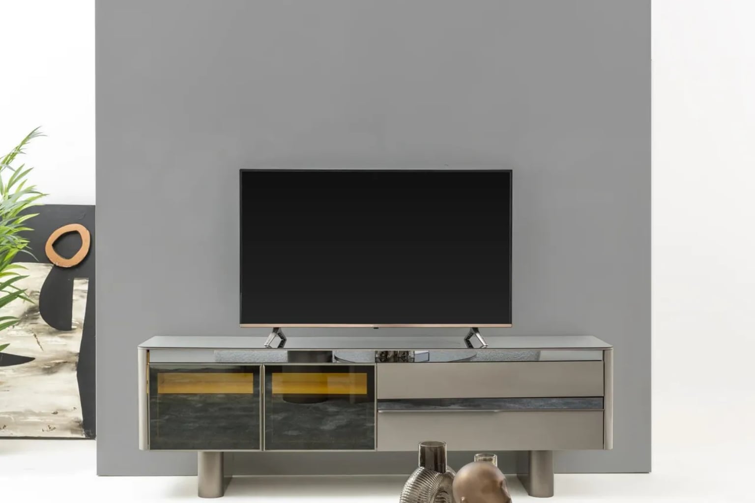 Modern ve zarif ahşap TV ünitesinin yer aldığı, doğal ışıkla aydınlanmış şık bir salonun fotoğrafı. Ünitenin üzerinde büyük bir televizyon ve minimalist dekoratif objeler bulunuyor.